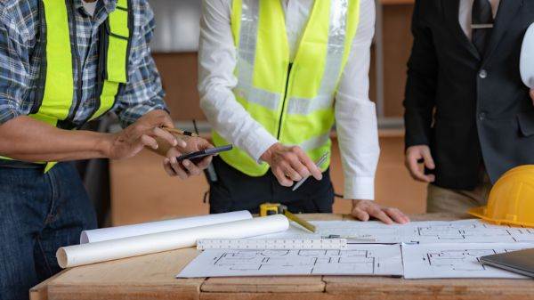 Construction and Contracting Service: Contractors discussing a project plan at a construction site.